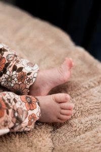 Detailfoto van de kleine voetjes van de baby in een broekje met bloemenprint.