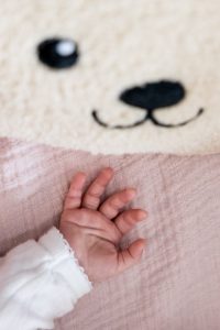 Detailfoto van het kleine handje van de baby dat een knuffelbeer vasthoudt