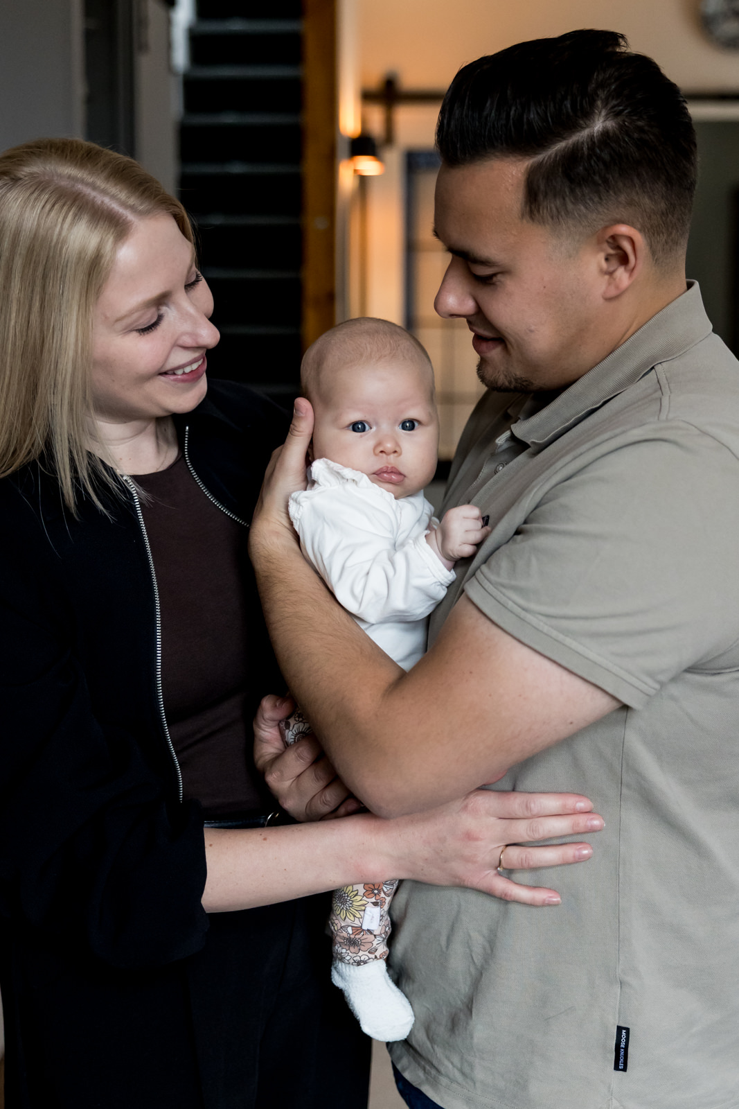 Baby zit tussen papa en mama in en krijgt een knuffel van beide ouders tegelijk.