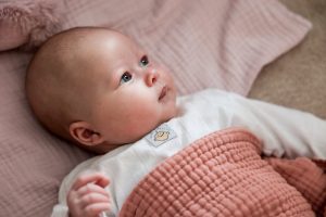 Baby Laurie ligt wakker op bed en kijkt nieuwsgierig rond in de woonkamer.
