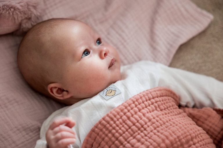 Baby Laurie ligt wakker op bed en kijkt nieuwsgierig rond in de woonkamer.