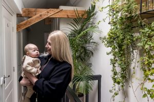 Moeder houdt haar babydochter in de woonkamer, omringd door groene planten en warme sfeer.