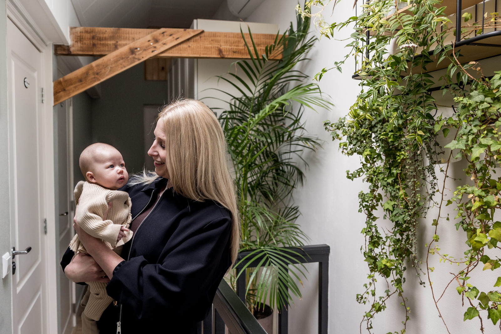 Moeder houdt haar babydochter in de woonkamer, omringd door groene planten en warme sfeer.