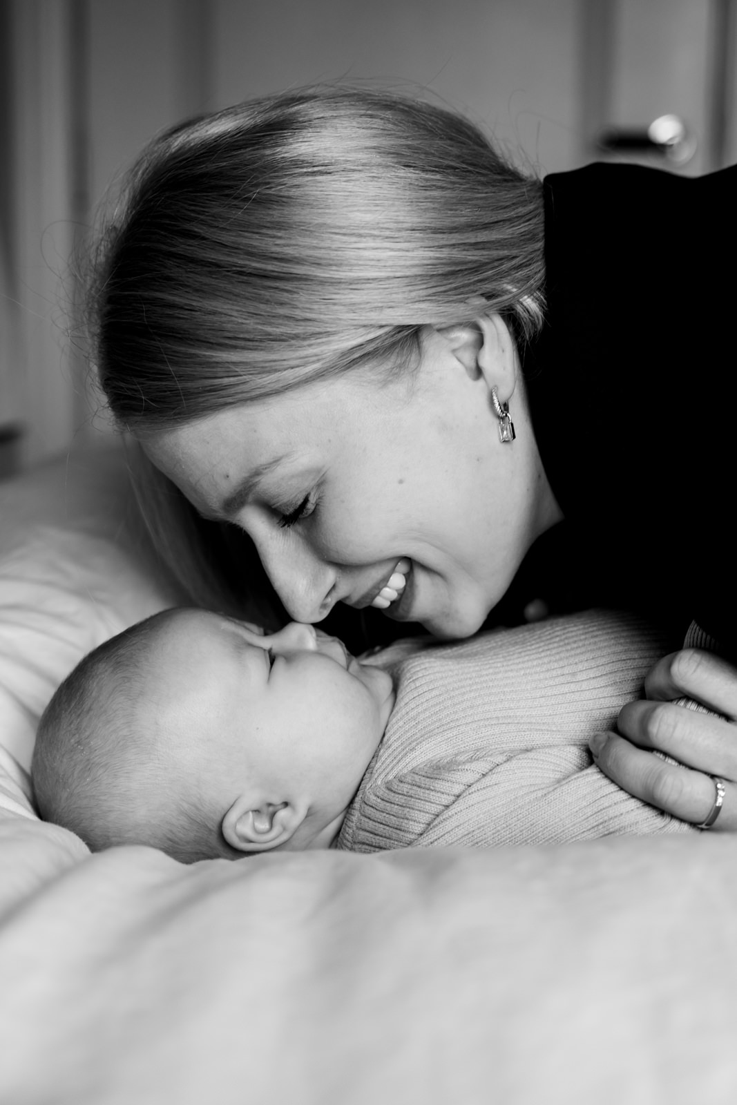 Zwart-wit foto van mama en baby op bed, met hun neuzen zachtjes tegen elkaar aan.