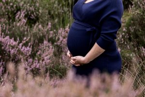 Close-up van de zwangere buik tussen de paarse heide op Het Leesten in Ugchelen, terwijl mama liefdevol haar buik vasthoudt.