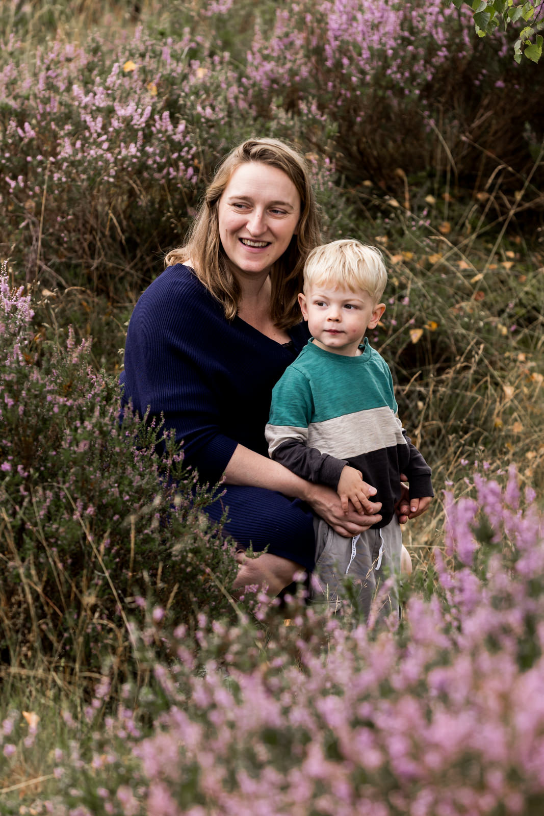 Mama en zoon tussen de heide op Het Leesten in Ugchelen, kijkend naar papa, terwijl mama haar zoon vasthoudt met een warme glimlach.